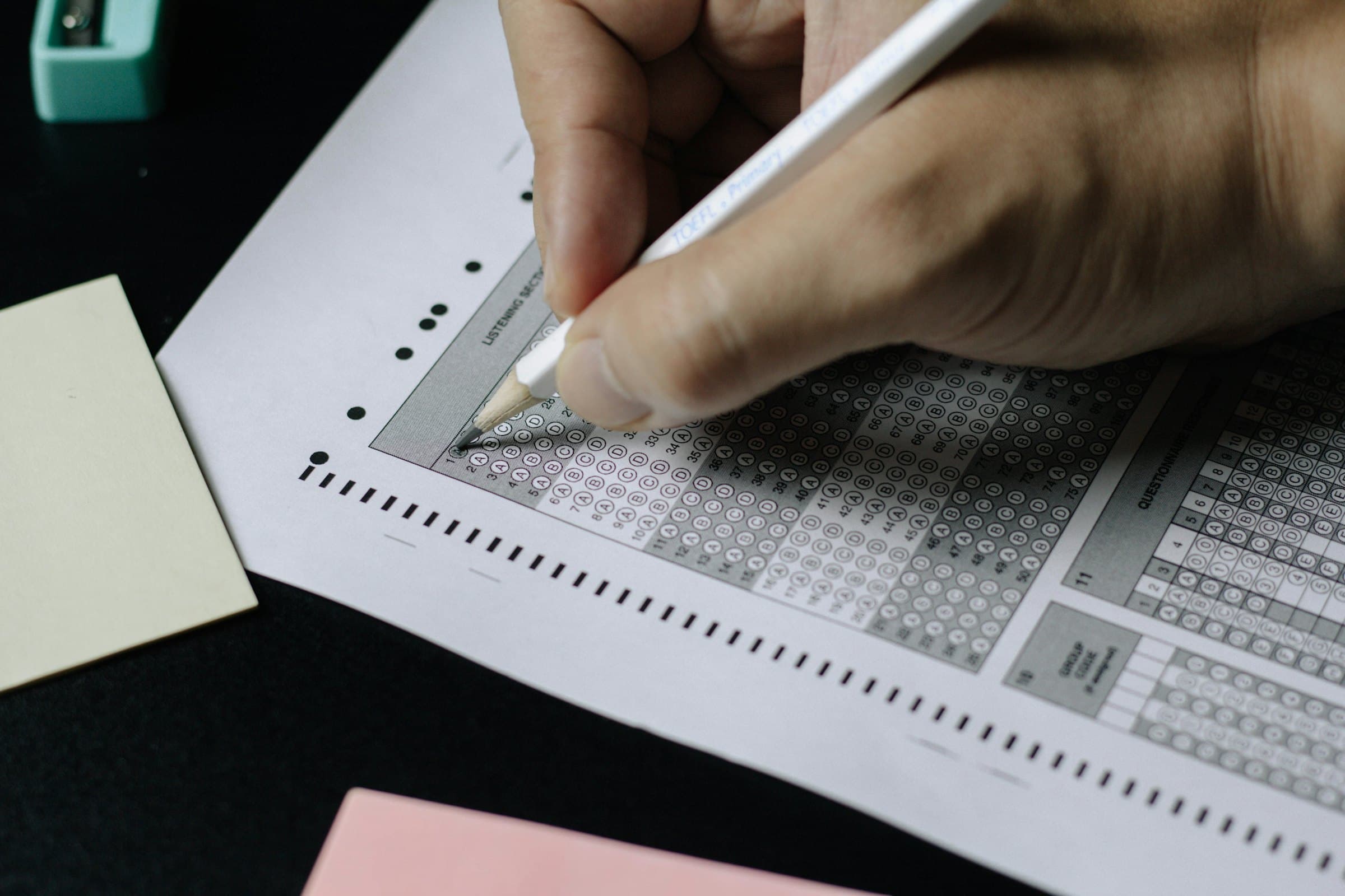 A hand filling in the bubbles of a printed answer sheet with a pencil